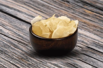 A bowl of white potato slices on a wooden table