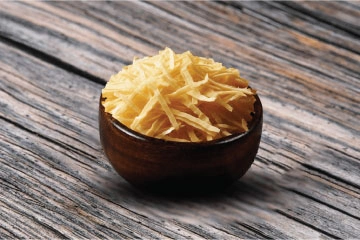 A bowl of white potato shreds on a wooden table